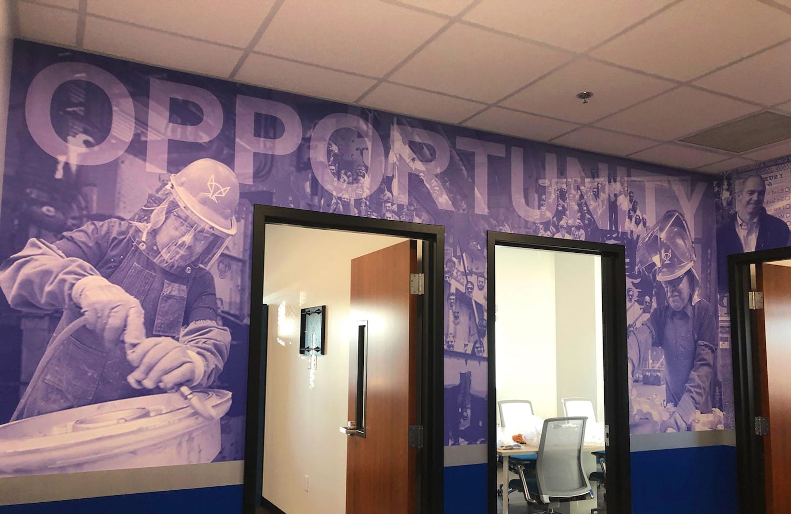Office corridor wall wrapped in a large printed mural with oversized typography over worker photography