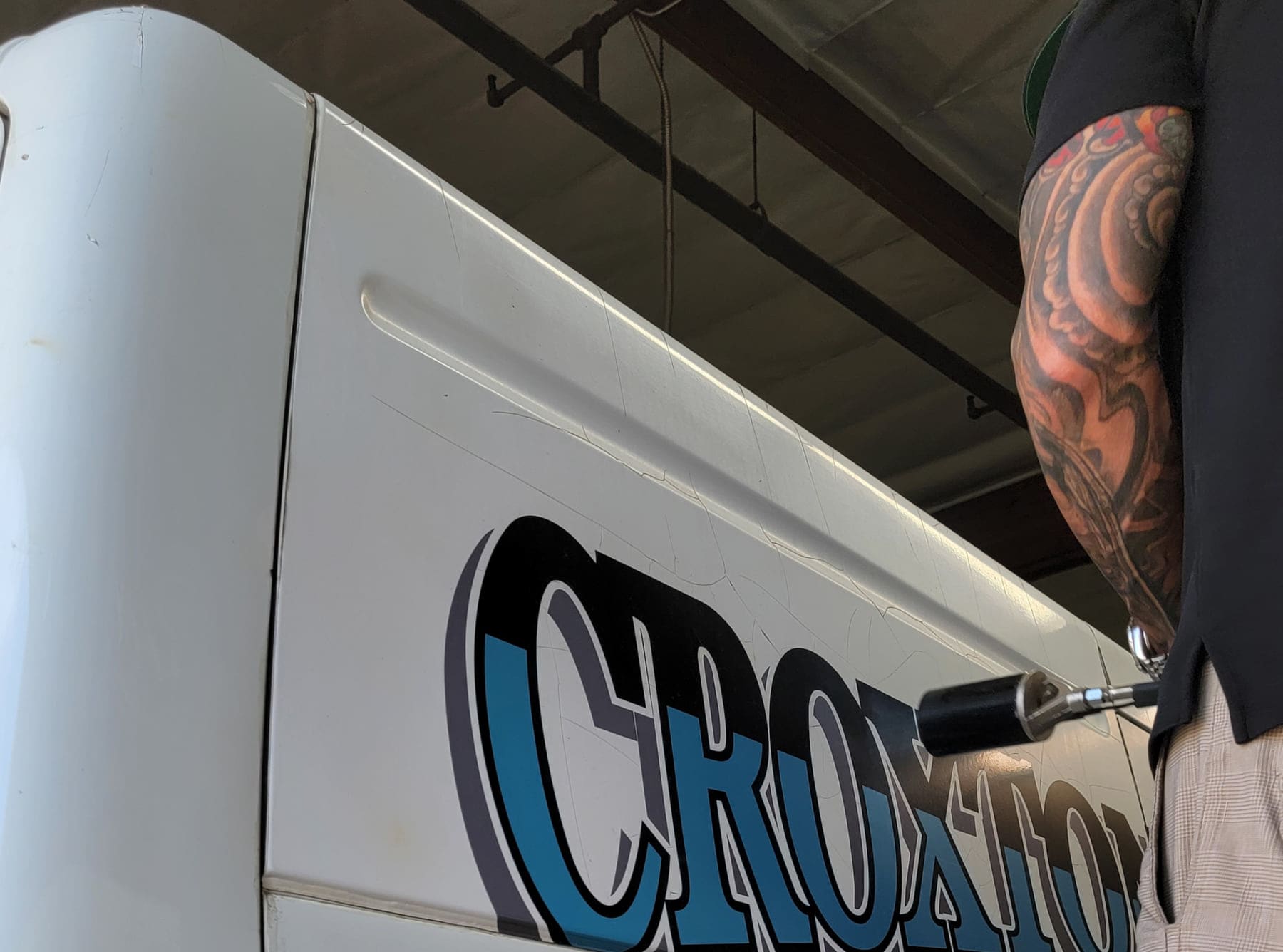 Technician pressure-washing old lettering off a vehicle panel during graphics removal