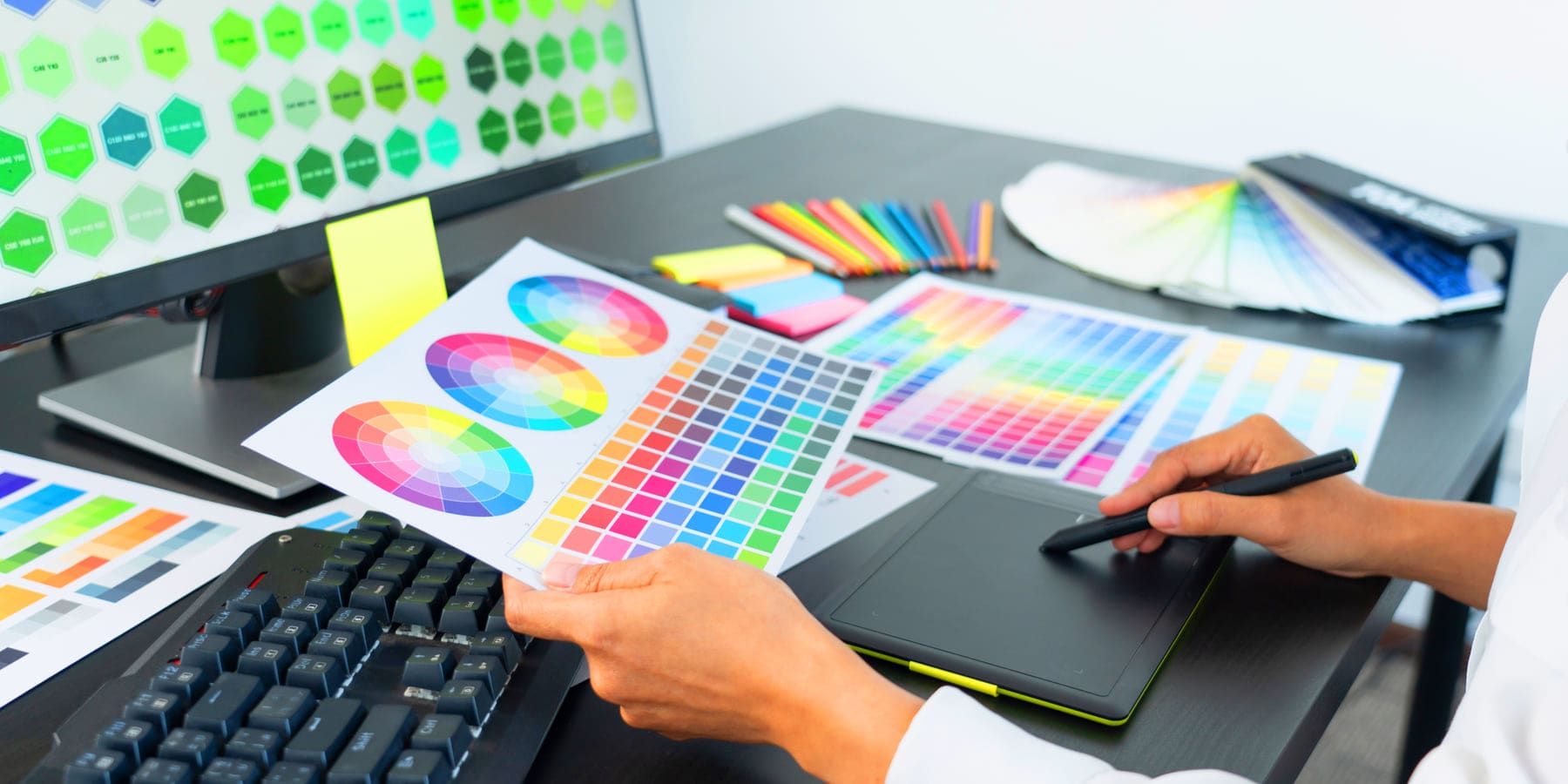 Designer matching print colors against Pantone fans, printed swatch charts, and a calibrated monitor